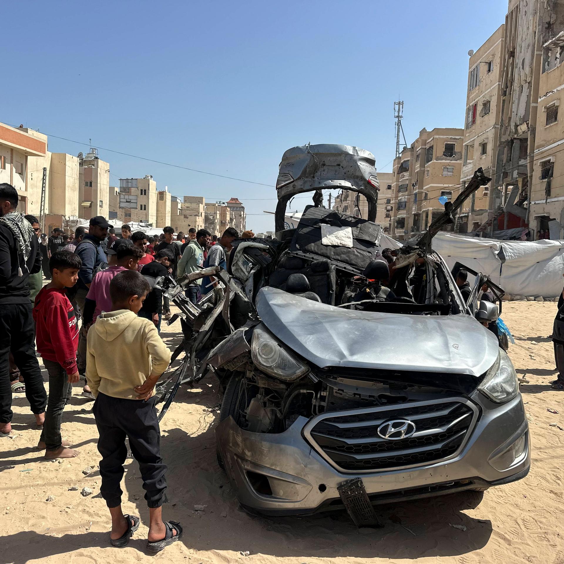Mehrere Menschen stehen um ein schwer beschädigtes Auto in der palästinensischen Stadt Chan Junis im Gazastreifen.