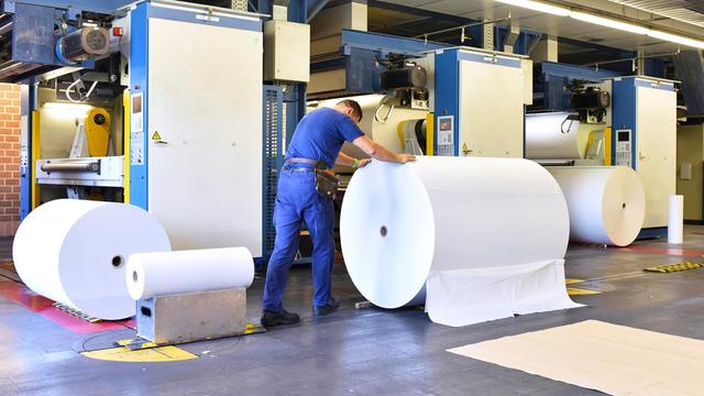 Ein Mann schiebt eine Papierrolle in einer Druckerei