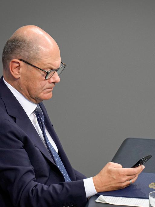 Bundeskanzler Olaf Scholz (SPD) hält im seitlichen Portrait auf der Regierungsbank sein Mobiltelefon in der Hand.