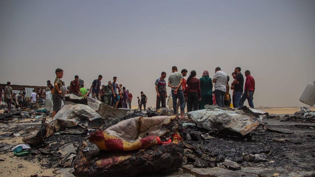 Angriff auf Rafah am 27.5.2024: das zerstörte Zeltlager, Menschen stehen im Hintergrund.