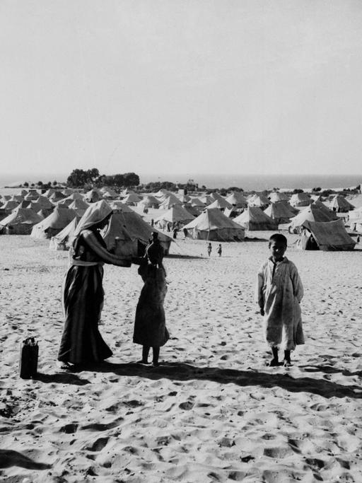 Eine Frau zeigt ihrer Tochter wie sie Wasser tragen kann. Die arabischen Flüchtlinge stehen 1949 vor einem Zeltcamp in Gaza. 