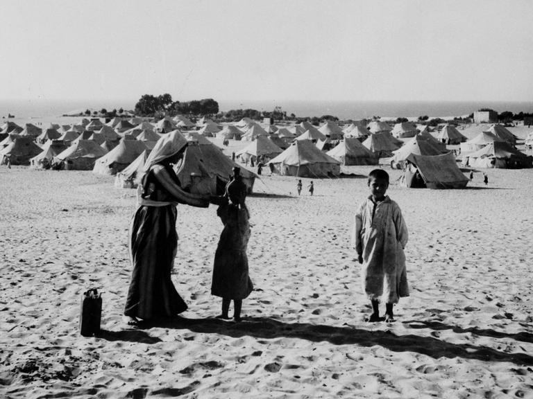Eine Frau zeigt ihrer Tochter wie sie Wasser tragen kann. Die arabischen Flüchtlinge stehen 1949 vor einem Zeltcamp in Gaza. 