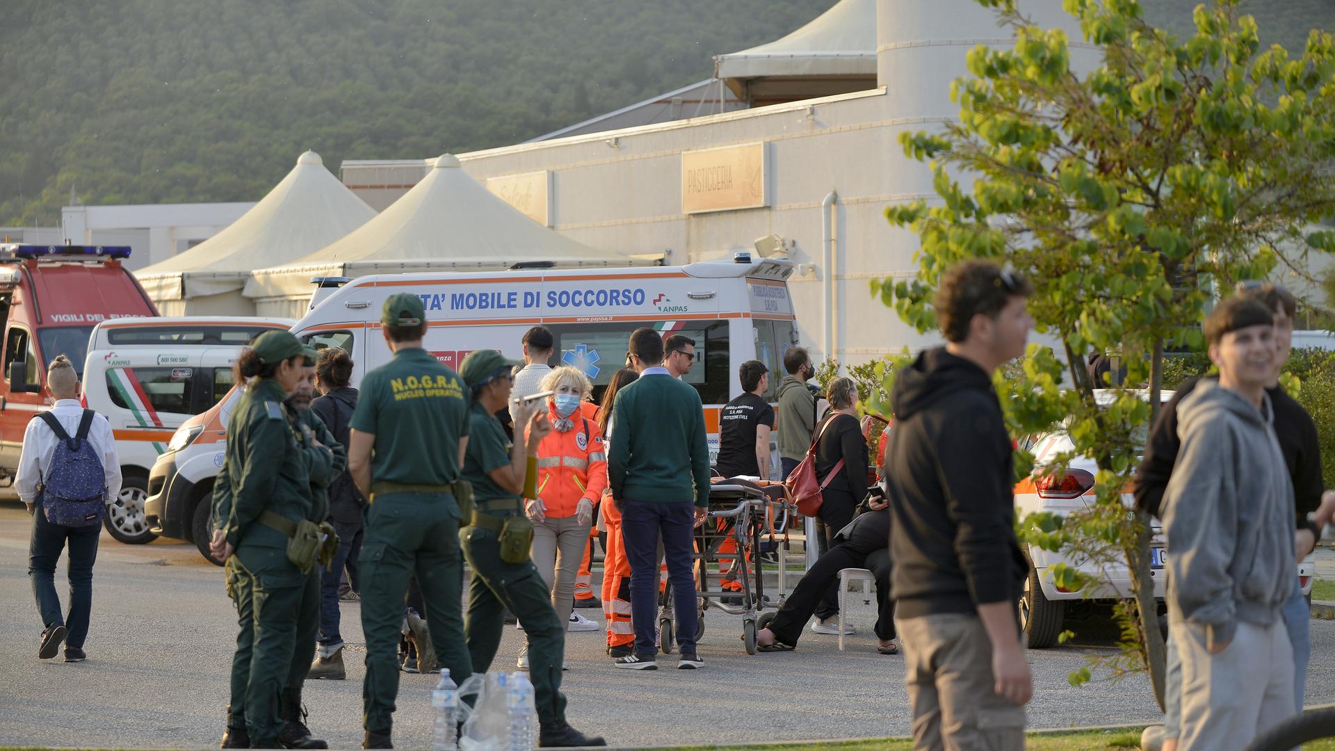 Mehrere Menschen stehen vor einer Reihe von weißen Zelten und Feuerwehrautos. Einige tragen Warnwesten