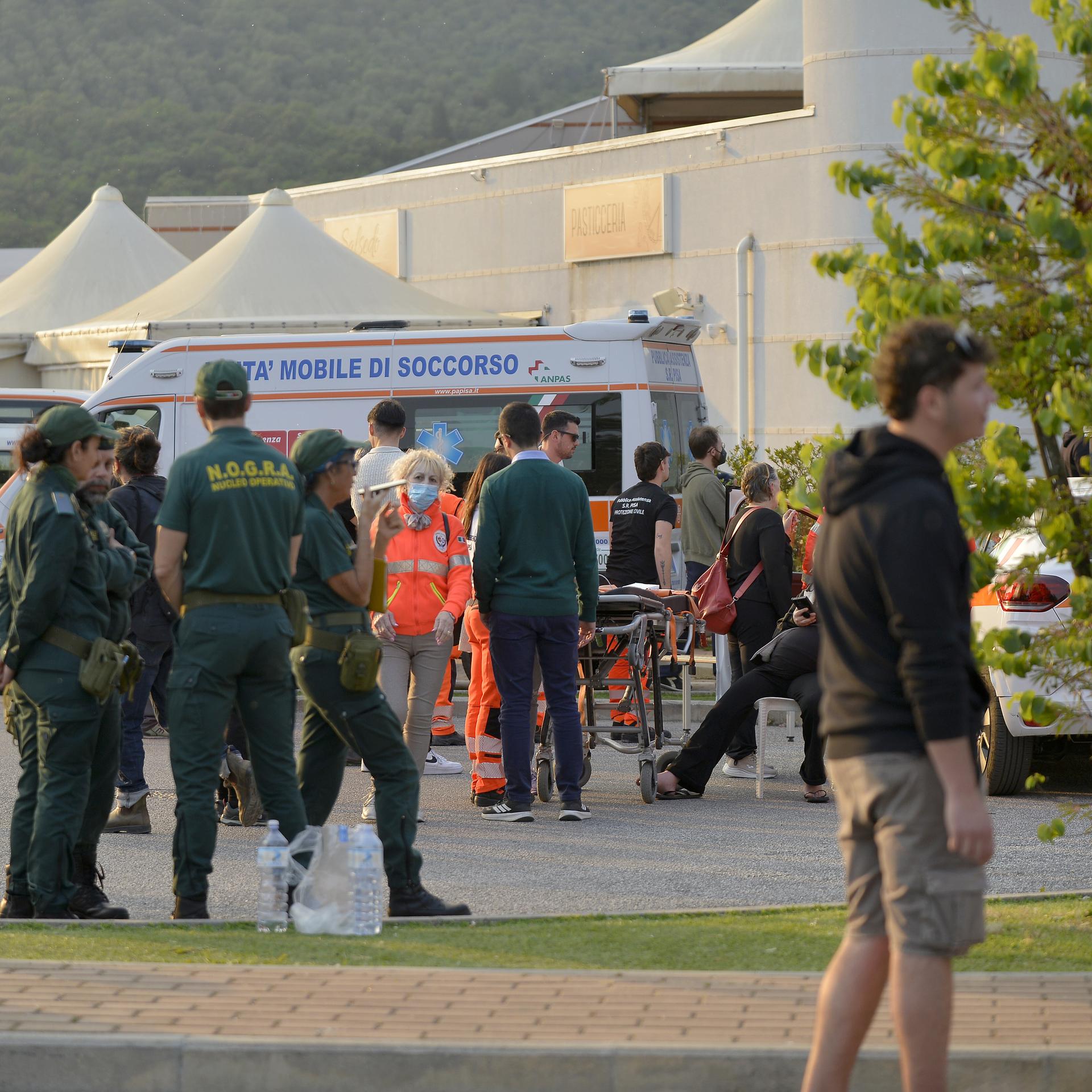 Mehrere Menschen stehen vor einer Reihe von weißen Zelten und Feuerwehrautos. Einige tragen Warnwesten