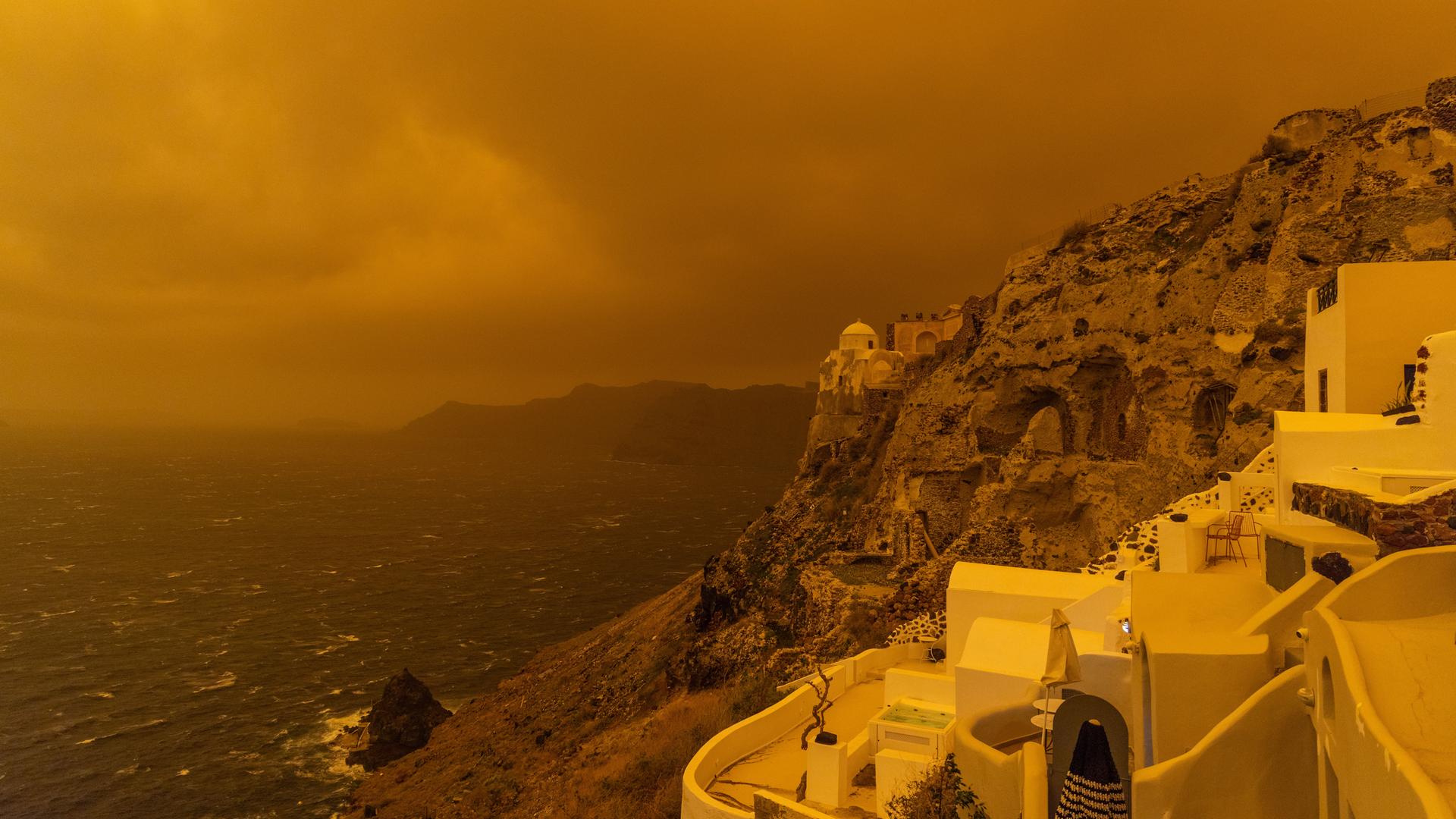 Kräftiger Sturm trägt Sand aus Afrika über die Insel Santorin und färbt den Himmel orangerot ein. 