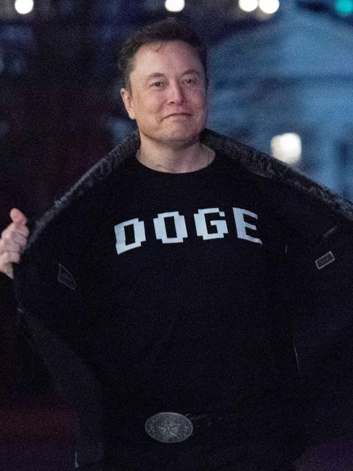 Elon Musk zeigt den Medien sein Oberteil mit der Aufschrift "DOGE", während er auf dem Südrasen des Weißen Hauses in Washington geht. 