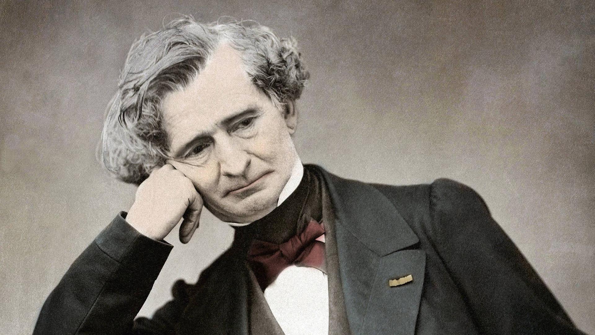 Der ältere Komponist Hector Berlioz sitzt auf einer nachkolorierten Fotografie versonnen auf einem Stuhl mit aufgestützen Kopf.