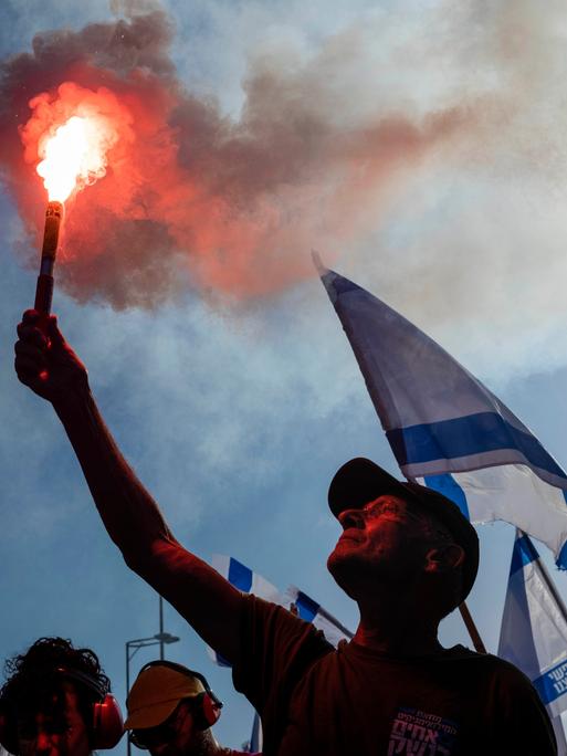 Israelische Demonstranten gegen die Justizreform blockieren eine Straße. Sie halten die israelisch Fahne hoch.