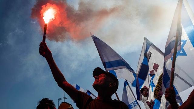 Israelische Demonstranten gegen die Justizreform blockieren eine Straße. Sie halten die israelisch Fahne hoch.