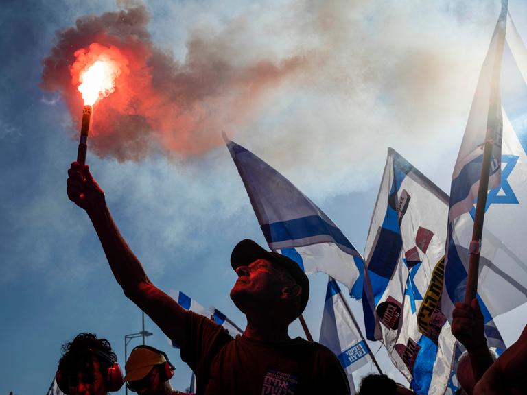 Israelische Demonstranten gegen die Justizreform blockieren eine Straße. Sie halten die israelisch Fahne hoch.