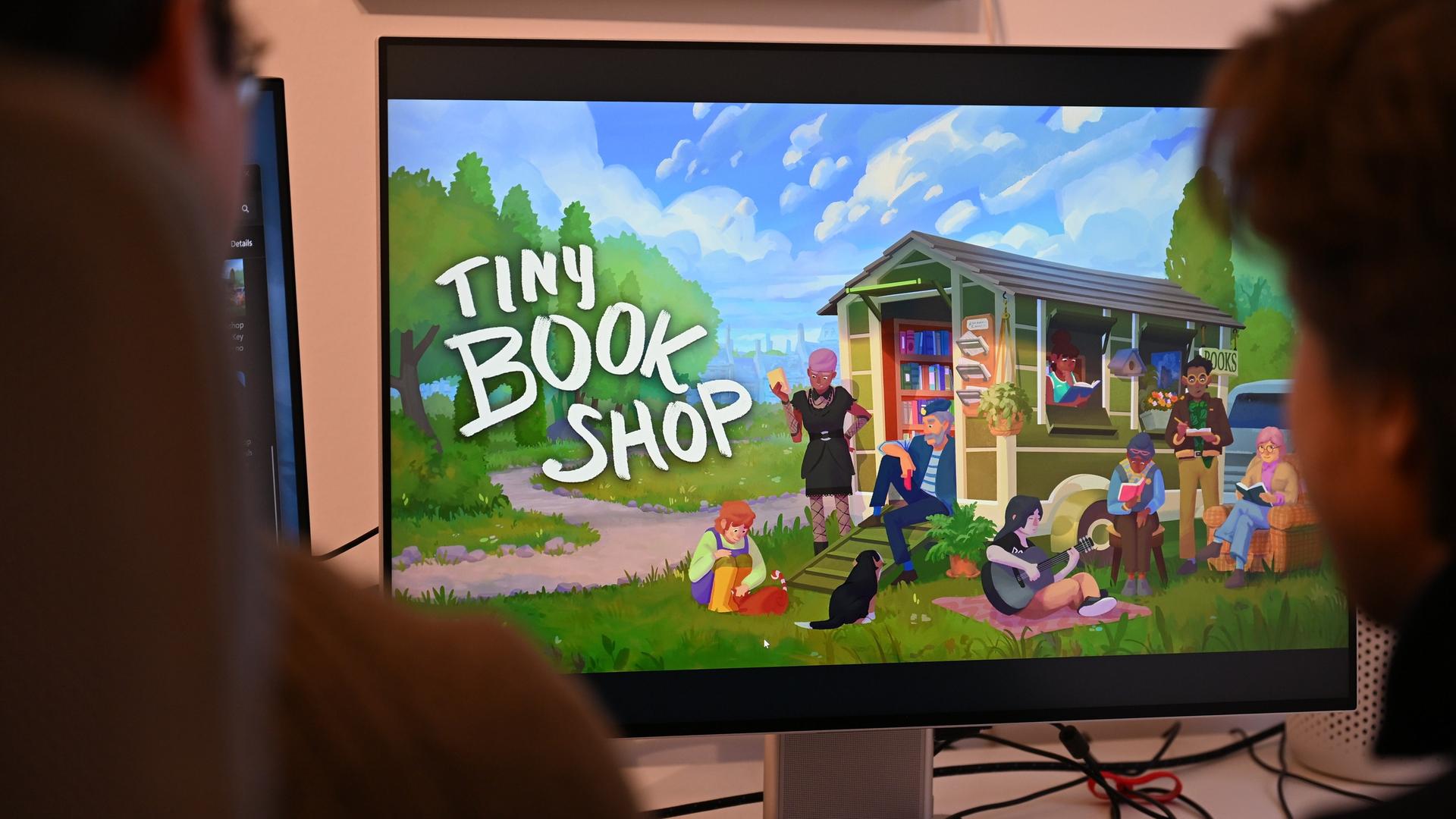 Zwei junge Männer sitzen vor einem Screen und blicken auf das Game "Tiny Bookshop". Zwei junge Männer sitzen vor einem Screen und blicken auf das Game "Tiny Bookshop".