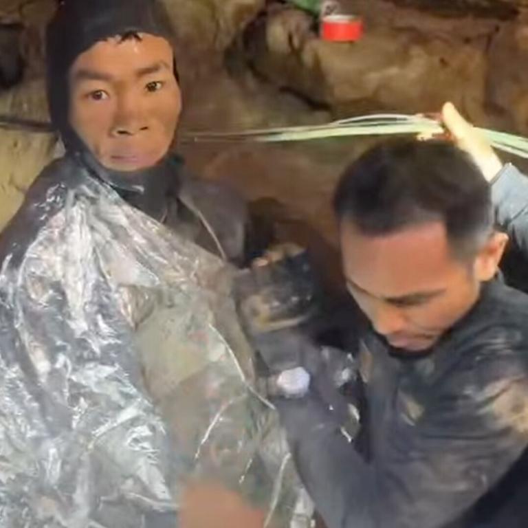 Der Mann trägt einen Neoprenanzug und ist in eine Wärmedecke gehüllt. Er schaut ernst in die Kamera. Neben ihm ein Mitglied des Rettungspersonals.