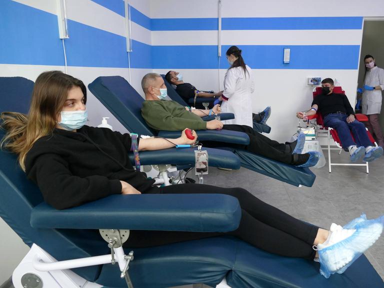 Frewillige spenden in Iwano-Frankiwsk in der Ukraine Bliut. Im Vordergrund ist eine Frau mit dunklen, langen Haaren zu sehen, die auf einem Sessel liegt. Sie hält einen roten Ball in ihrer Hand zusammendrückt, in ihrer Ellenbeuge hat sie eine Kanüle stecken. im Hintergrund liegen mehr Menschen auf solchen liegen, zudem ist medizinisches Personal im Bild.