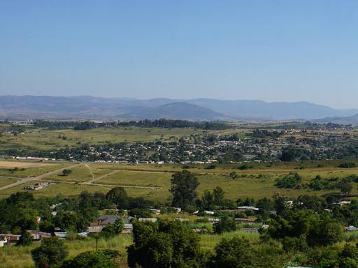 Blick auf Landschaft und Lubombo-Berge im Königreich Eswatini. Eine große grüne Fläche, im Hintergrund sind Berge und ein heller blauer Himmel zu sehen. 