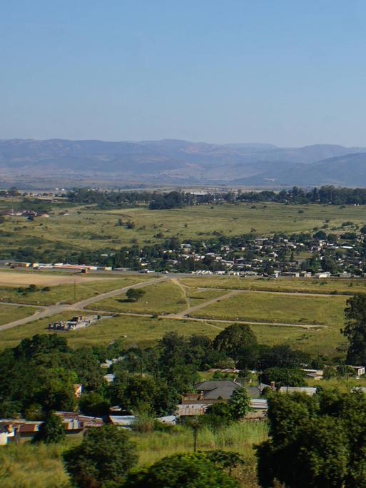 Blick auf Landschaft und Lubombo-Berge im Königreich Eswatini. Eine große grüne Fläche, im Hintergrund sind Berge und ein heller blauer Himmel zu sehen. 