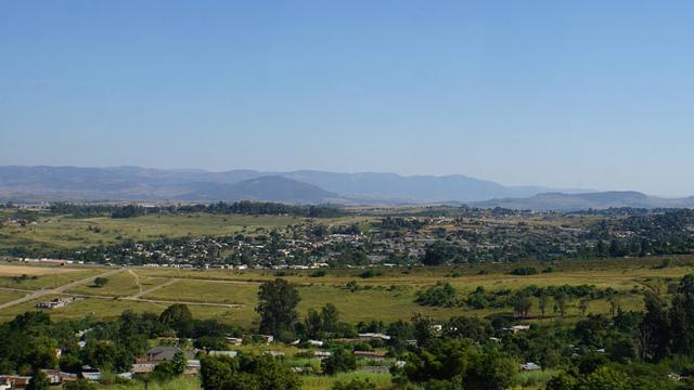 Blick auf Landschaft und Lubombo-Berge im Königreich Eswatini. Eine große grüne Fläche, im Hintergrund sind Berge und ein heller blauer Himmel zu sehen. 