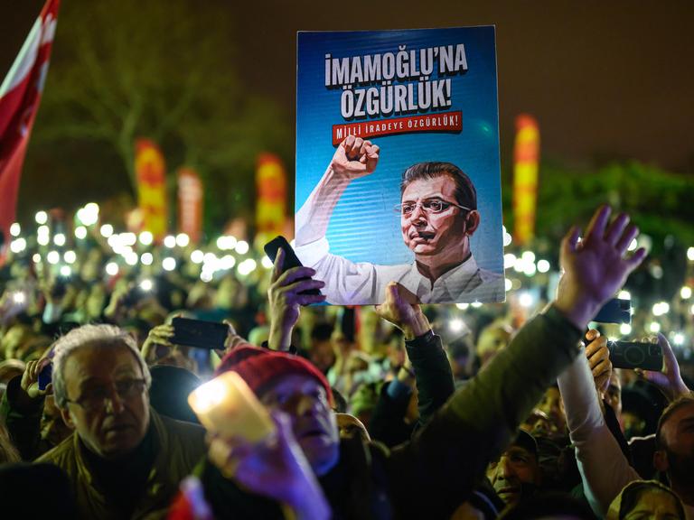 Demonstranten halten bei einem Protest ein Poster von Ekrem Imamoğlu in die Höhe.