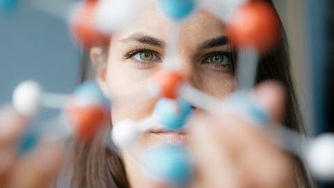 Eine Frau schaut durch ein blau-rotes DNA-Modell.