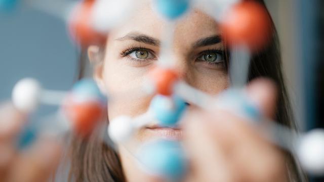 Eine Frau schaut durch ein blau-rotes DNA-Modell.