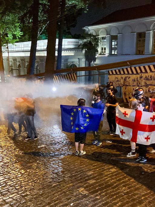 Demonstrierende in Tiflis halten georgische und EU-Flaggen hoch, während sie von der Polizei mit Wasser beschossen werden.