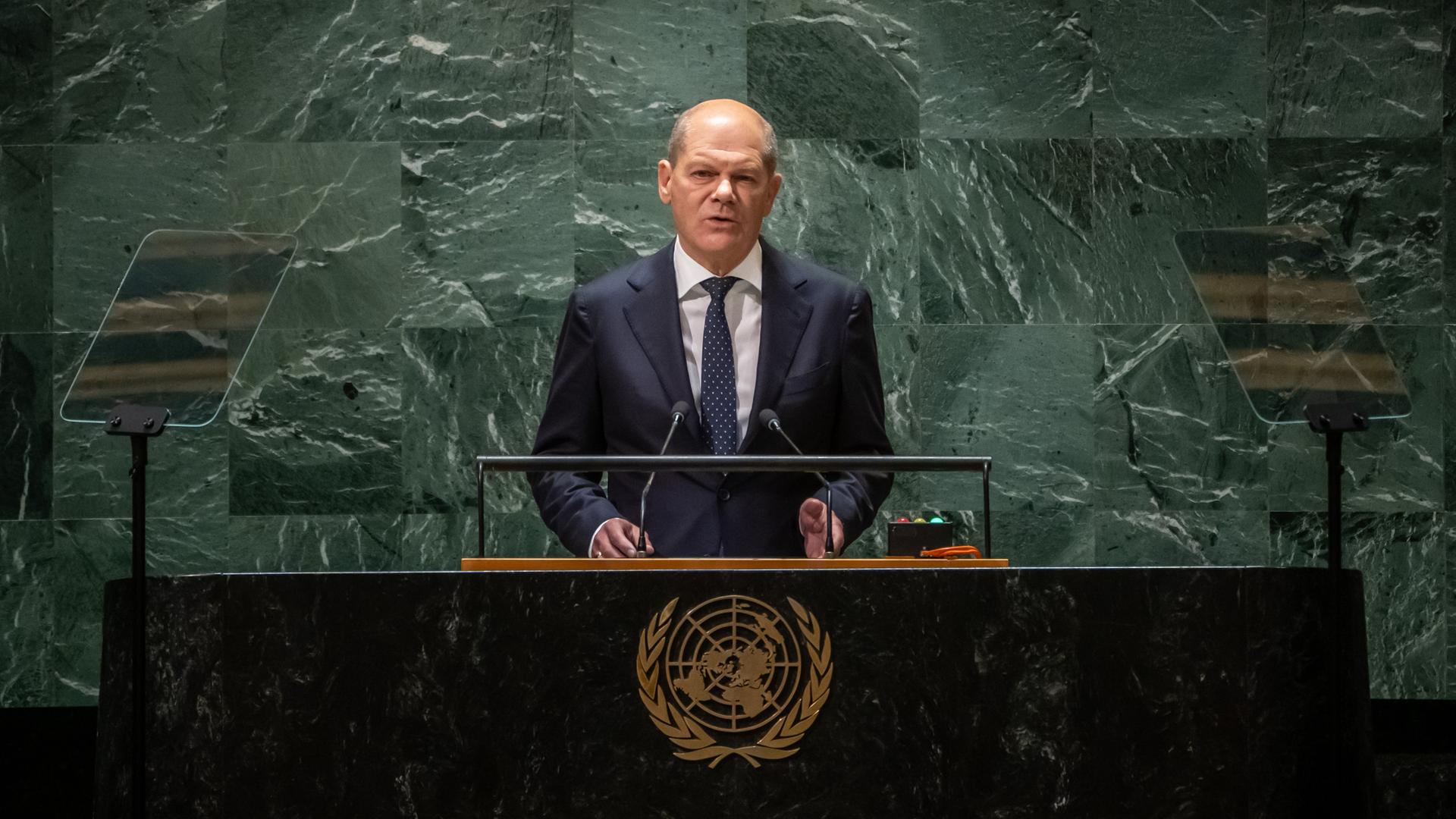 Bundeskanzler Olaf Scholz steht im Plenum der UNO-Vollversammlung am Redepult, im Hintergrund schimmert die für den Ort typische grünliche Wand.