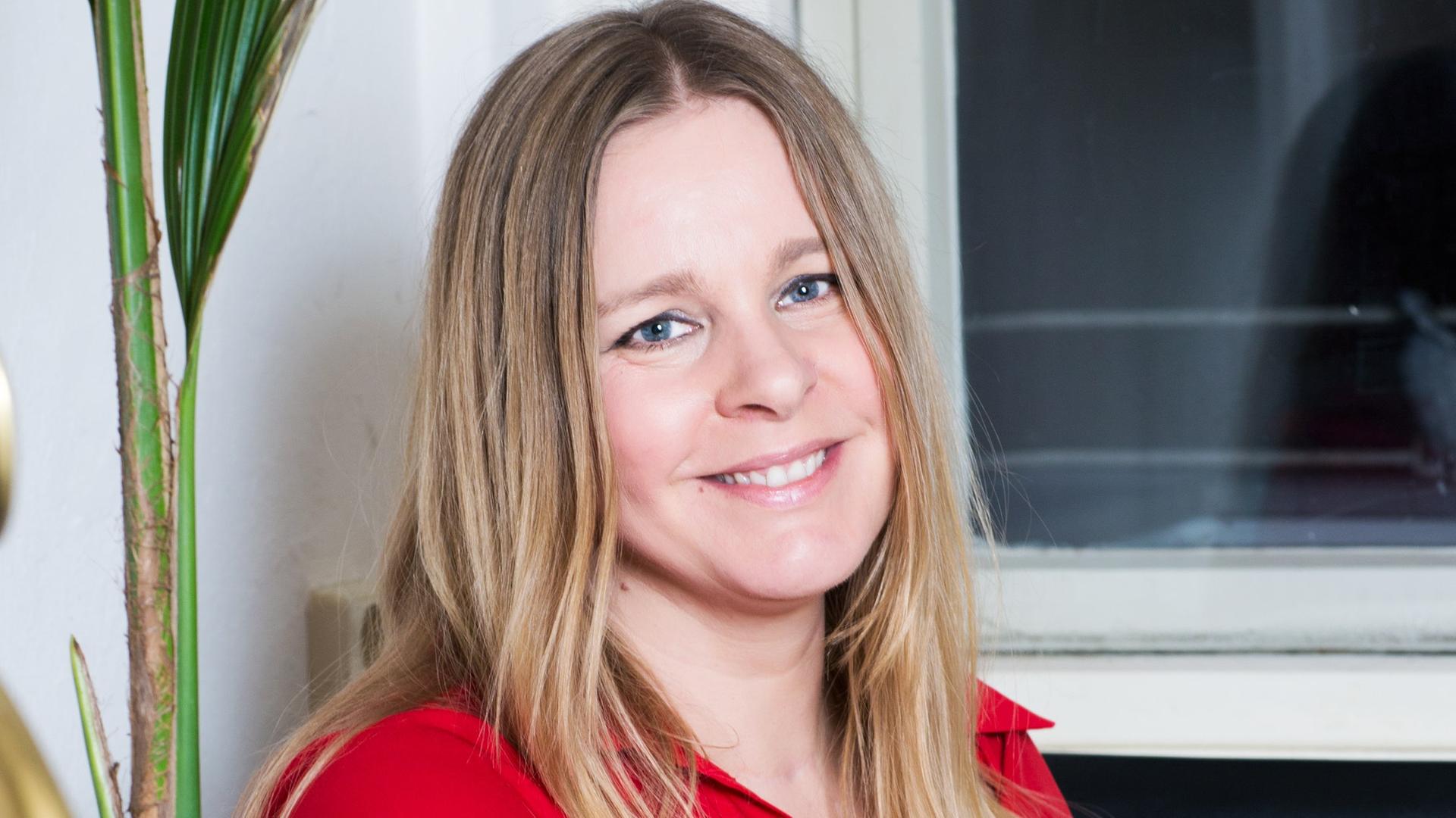 Porträt von Stefanie Hofeditz. Sie sitzt in einer roten Bluse an einem Tisch und stützt ihren Arm auf einen Stapel Kochbücher. Porträt von Stefanie Hofeditz. Sie sitzt in einer roten Bluse an einem Tisch und stützt ihren Arm auf einen Stapel Kochbücher.