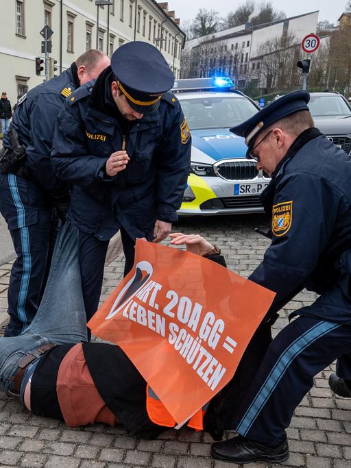 Polizisten zerren einen Aktivisten der Klimaschutzbewegung "Letzten Generation" von einer Straße in der Innenstadt von Passau, Bayern.