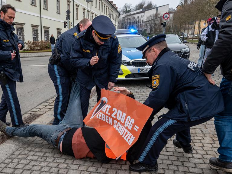 Polizisten zerren einen Aktivisten der Klimaschutzbewegung "Letzten Generation" von einer Straße in der Innenstadt von Passau, Bayern.