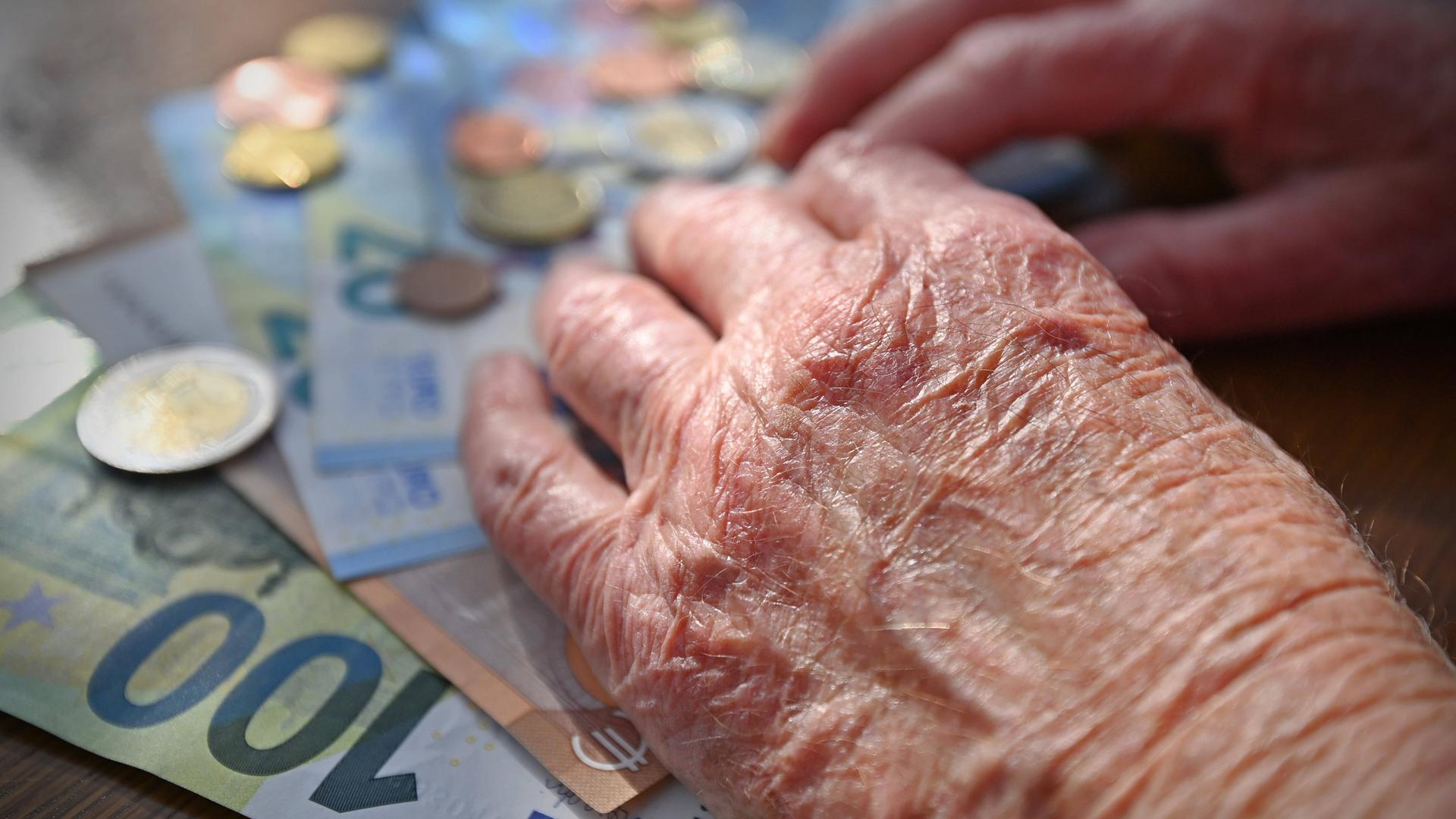 Hände einer alten Frau, darunter ein paar Geldscheine und Münzen.