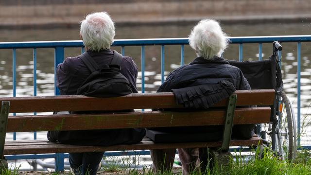 Senioren sitzen auf einer Parkbank am Fluss.