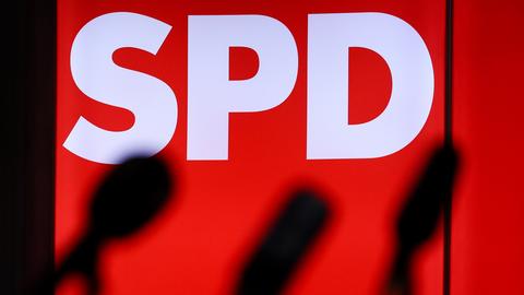 Mikrofone stehen vor einer leuchteten Wand mit dem Logo der Partei SPD.