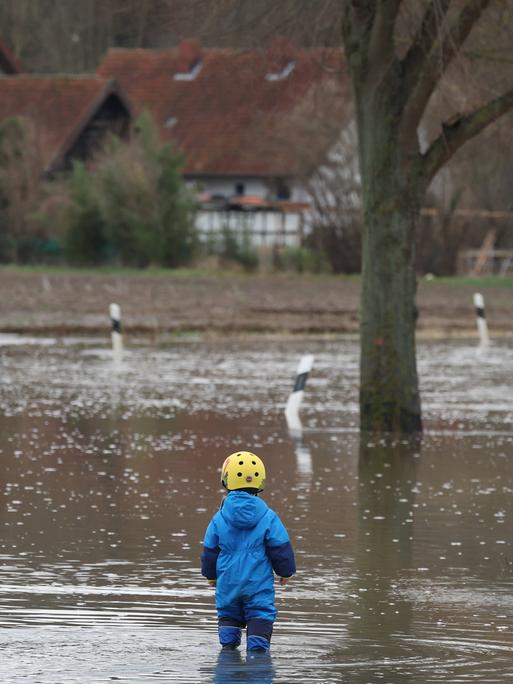 Lauenstadt bei Schulenburg (Region Hannover) ist im Dezember 2023 vom Hochwasser eingeschlossen. Ein Kleinkind in Gummistiefeln steht am Rand einer Straßenüberflutung, daneben ragt ein Verkehrsschild aus dem Wasser.