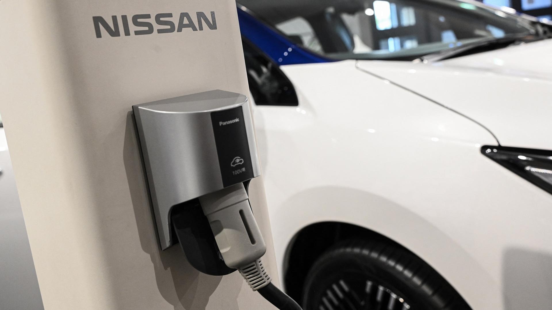 Ein weißes Auto wird an einer Nissan-Säule aufgeladen. Ein weißes Auto wird an einer Nissan-Säule aufgeladen.