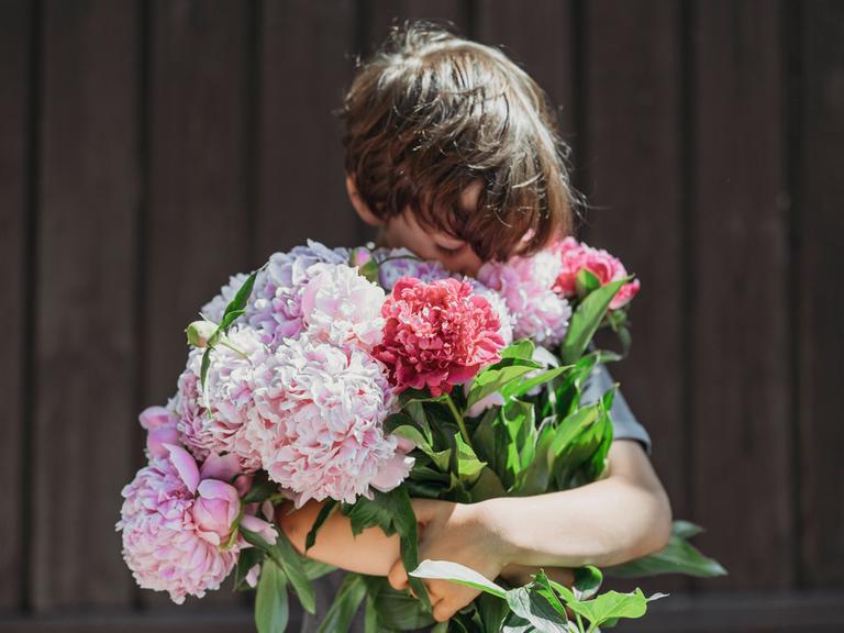 Ein Junge taucht sein Gesicht in einen großen Blumenstrauß.