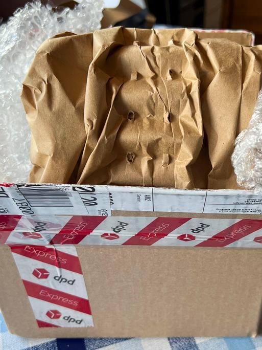Ein ausgepackter Karton steht auf einem Tisch. Im Karton liegt Luftpolsterfolie.