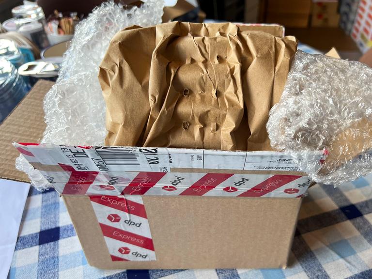 Ein ausgepackter Karton steht auf einem Tisch. Im Karton liegt Luftpolsterfolie.
