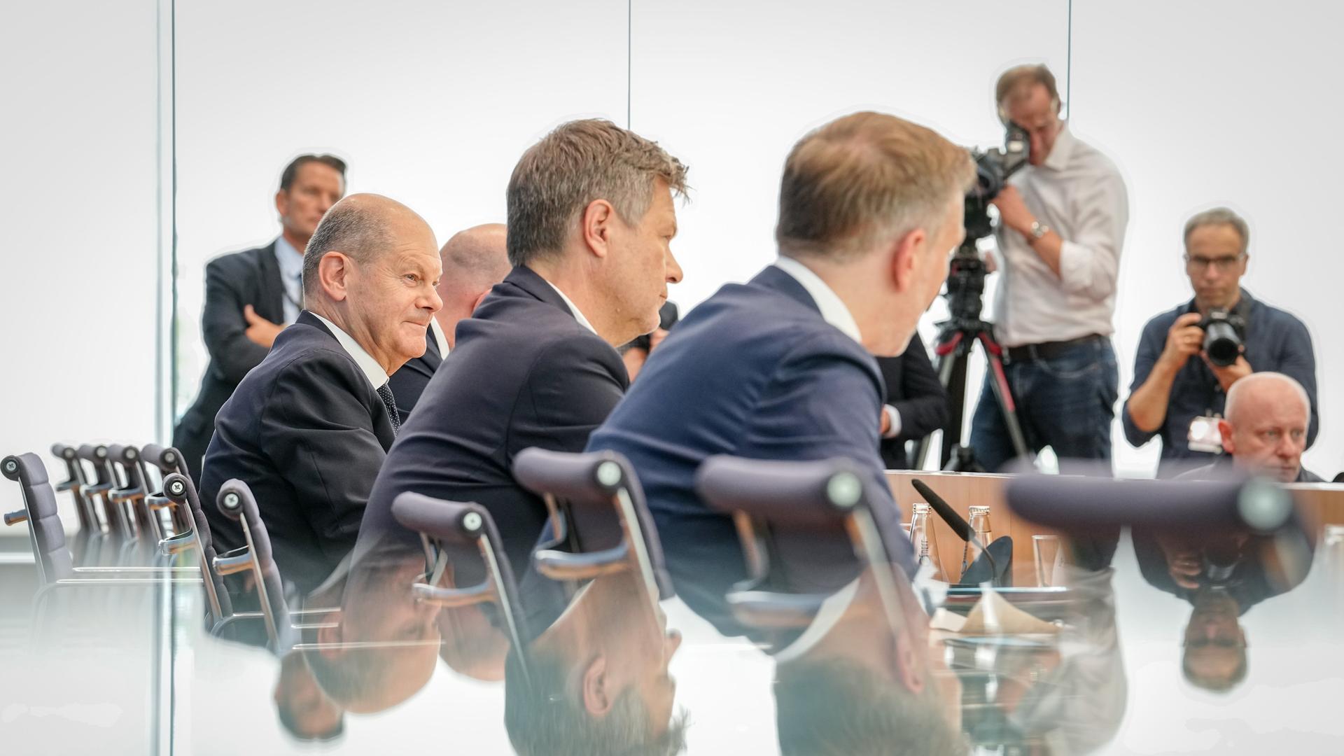 Bundeskanzler Olaf Scholz (SPD, l-r), Robert Habeck (Bündnis 90/Die Grünen), Bundesminister für Wirtschaft und Klimaschutz, und Christian Lindner (FDP), Bundesminister der Finanzen, sitzen bei einer Pressekonferenz zum Haushaltsplan 2025 nebeneinander. 