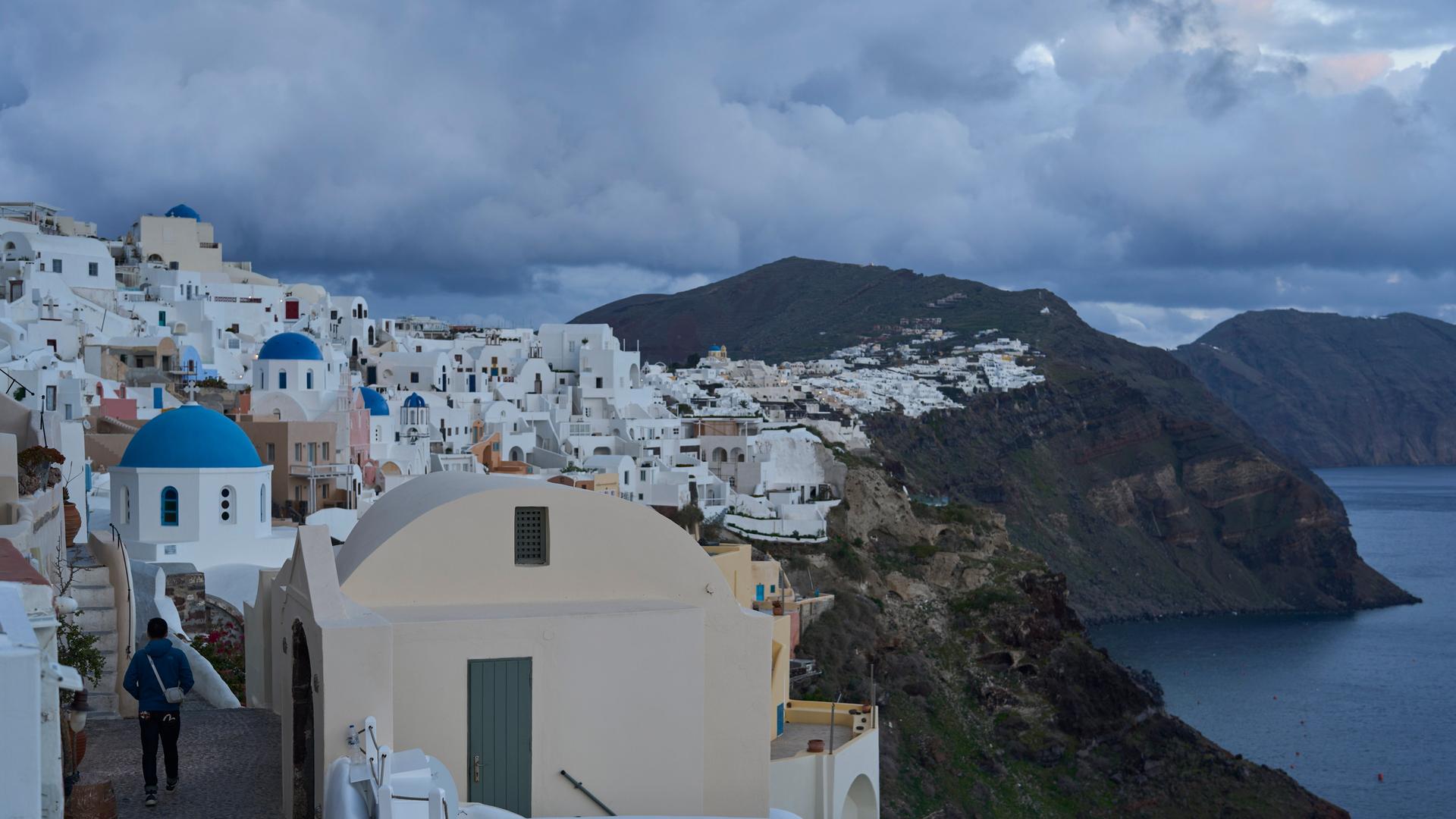 Ein Tourist nähert sich einer orthodoxen Kirche mit blauer Kuppel in Oia auf der erdbebengeschädigten Insel Santorini. 