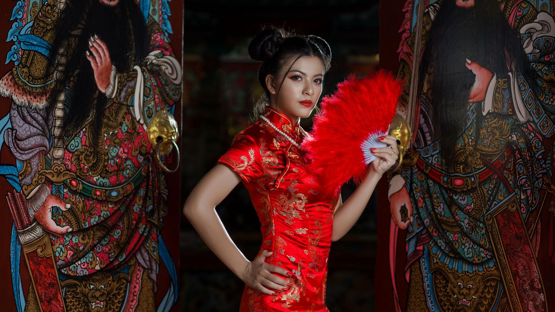 Eine stark gestylte Frau in traditionellem chinesischen roten Kleid und rotem Fächer.