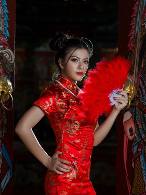 Eine stark gestylte Frau in traditionellem chinesischen roten Kleid und rotem Fächer.