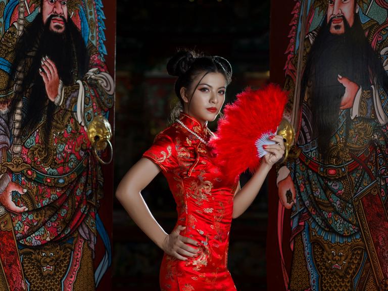 Eine stark gestylte Frau in traditionellem chinesischen roten Kleid und rotem Fächer.