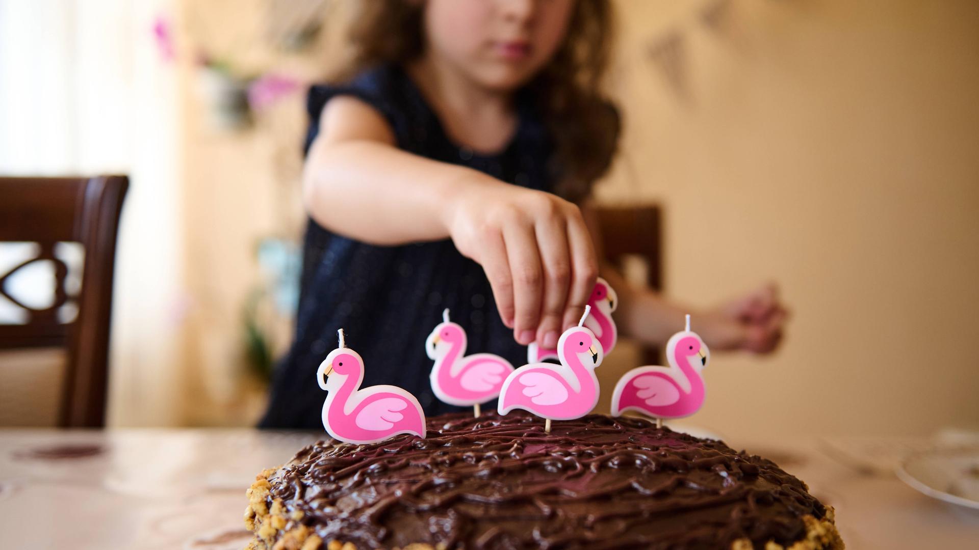 Ein Mädchen dekoriert eine Torte mit Flamingokerzen Ein Mädchen dekoriert eine Torte mit Flamingokerzen