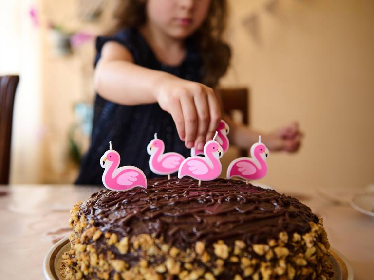 Ein Mädchen dekoriert eine Torte mit Flamingokerzen