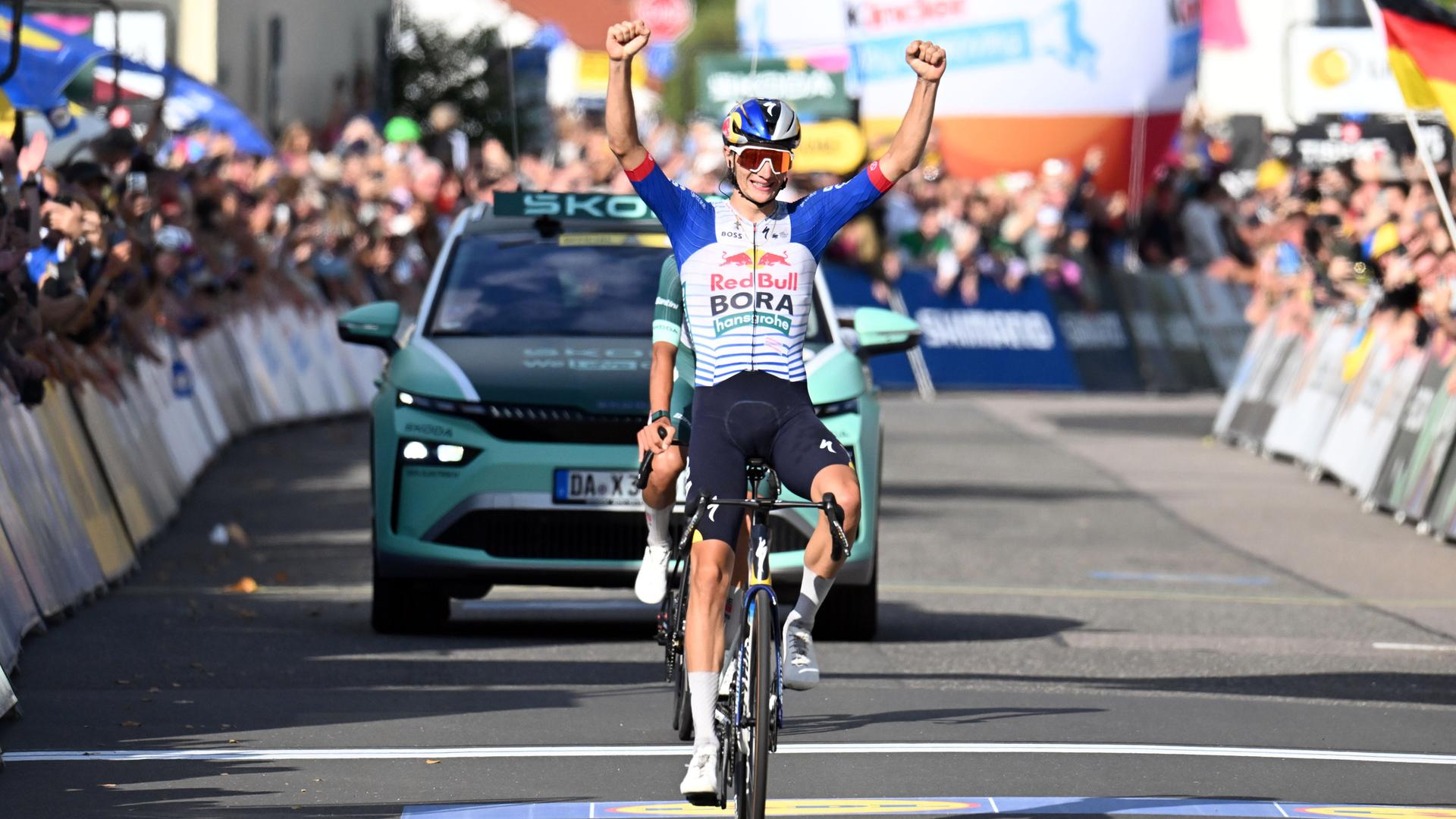 Giulio Pellizzari fährt auf dem Rennrad über die Ziellinie und hebt seine Arme jubelnd in die Höhe.