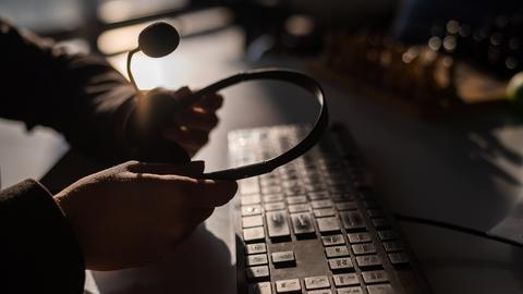 Dunkles Bild: Zwei Hände halten ein Headset über einer Tastatur.