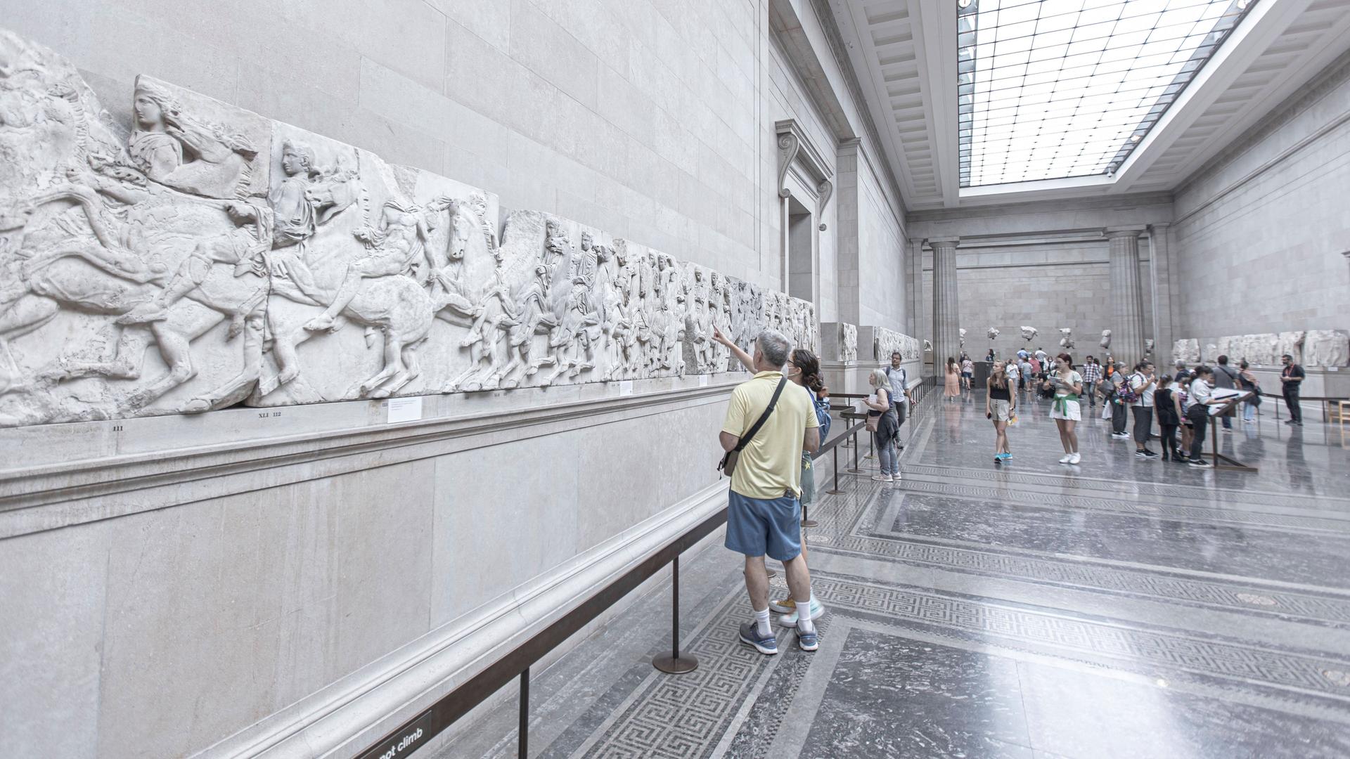 Besucher im British Museum in London betrachten Teile des Parthenon-Frieses, die an der Wand angebracht sind.