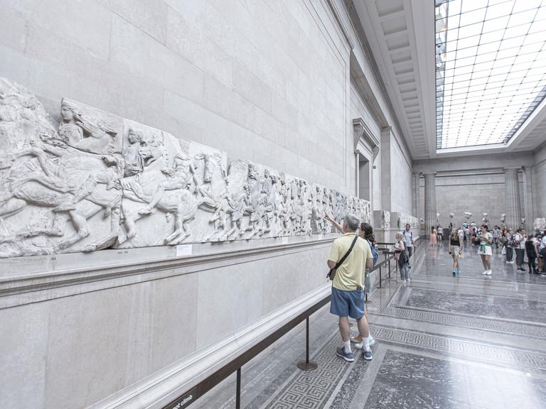 Besucher im British Museum in London betrachten Teile des Parthenon-Frieses, die an der Wand angebracht sind.