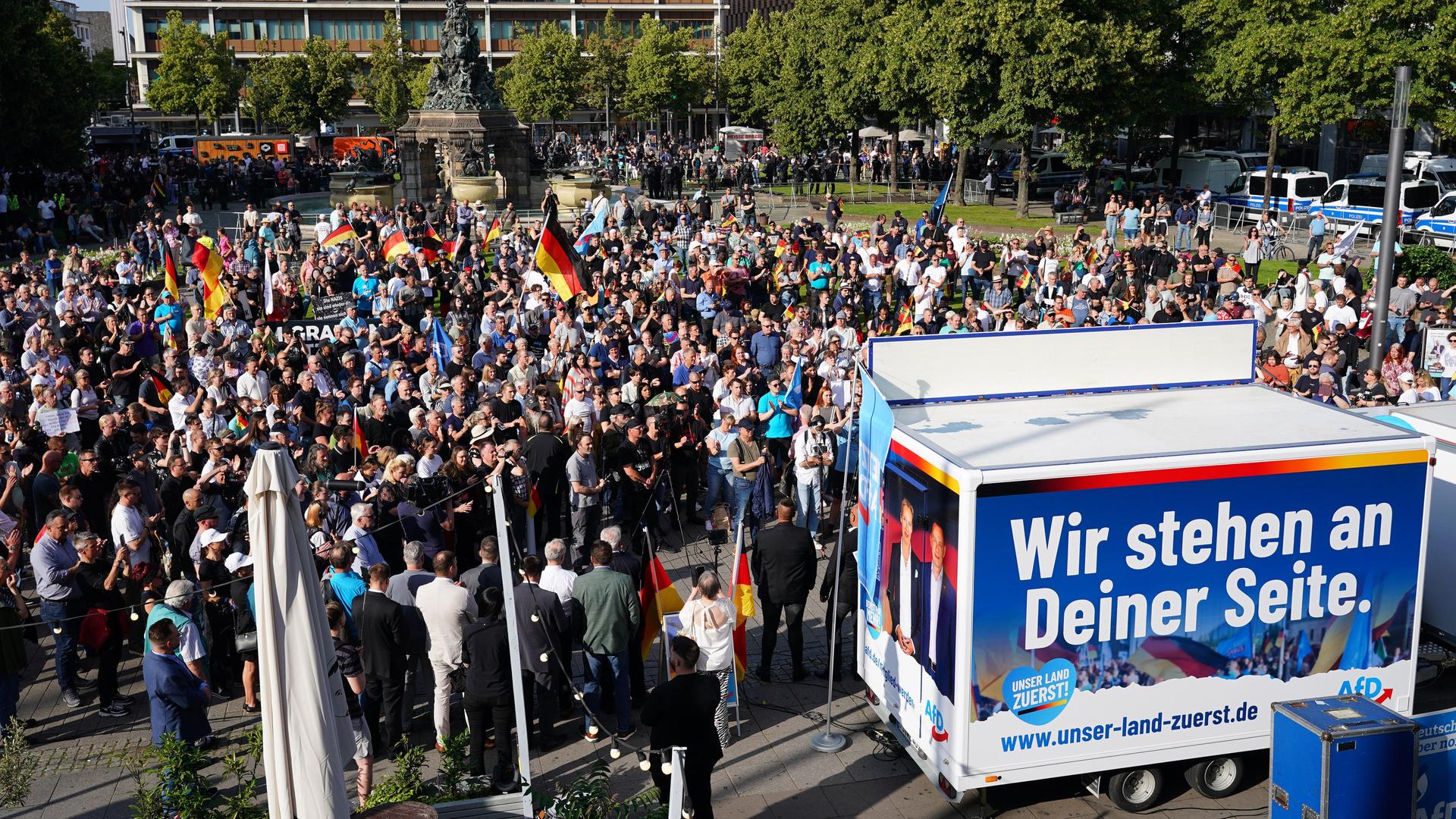 Teilnehmer einer Demonstration stehen auf einem öffentlichen Platz. Manche schwenken Deutschland-Flaggen.