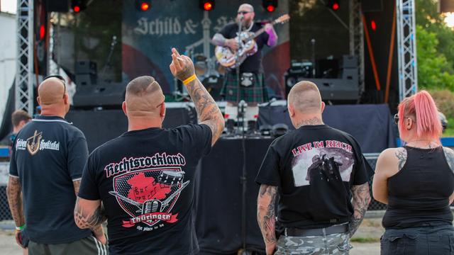 4 Personen stehen bei einem Konzert vor der Bühne. Auf einem Tshirt steht "Rechtsrock-Land".