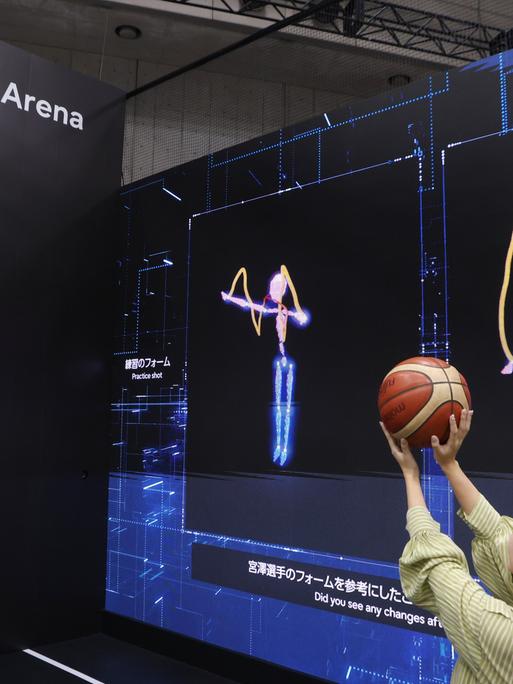 In Tokio stellte Fujitsu auf der Ceatec International im Oktober eine KI-Technologie vor, die beim Basketball Würfe analysiert und vergleicht. Zu sehen ist eine Frau, die vor Videoleinwänden auf einen Korb wirft.  